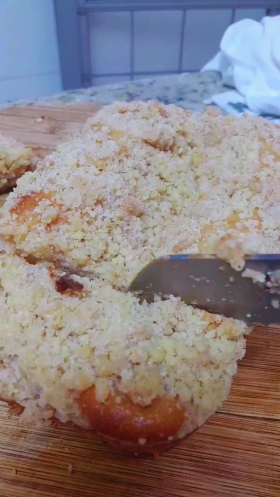 Cuca doce sendo cortada, com recheio cremoso e farofa por cima
